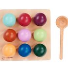 Neun bunte Kugeln auf einem Holzbrett. Rechts ein Holzlöffel. Texthinweis: "montessori by Eichhorn".