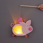 Ein rosa Papierlampion in Form eines Schweins, leuchtend mit einem Henkel, wird von einer Hand gehalten.