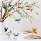 Keine Texte vorhanden. Ein Zweig mit Filzschmetterlingen und bemalten Eiern. Weiße Vase und Geschirr darunter.