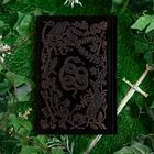 Keine erkennbaren Texte. Ein schwarzes Buch mit golddetaillierter Schlangen- und Naturillustration, umgeben von Pflanzen.