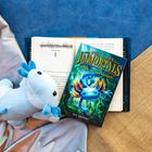 "The Last Immortals: Dawn of the Axolotl" Buch und axolotl-Plüschtier auf Stoff. Kapitel 1 eines Buches sichtbar.