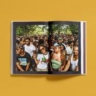 Offenes Buch mit einem Foto: Menschenmenge bei einem Outdoor-Event, Sonne, viele Menschen lächelnd und redend.