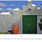 Texte: "Haus auf Lanzarote", "SALIDA DE EMERGENCIA". Grüne Tür in weißer Wand, große Tonvase, blauer Himmel.