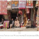 Taroudant, Souk. Männer sitzen umgeben von farbenfrohen Teppichen und Mustern vor einem Teppichladen.