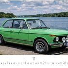 "BMW 1502", "ERB 0200" auf Kennzeichen. Ein grünes Auto am Seeufer, umgeben von Wald. Klarer Himmel mit Wolken.