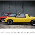 "Porsche 914", Gelber Sportwagen vorne, rote und silberne dahinter; Pflastersteine, dunkle Wand im Hintergrund.
