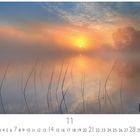 Kalender zeigt November. Sonnenaufgang über einem nebligen See mit schilfbewachsenen Ufern und Bäumen im Hintergrund.