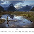 "Milford Sound" steht links unten. Eine beeindruckende Berglandschaft mit Wolken und einem spiegelnden Gewässer im Vordergrund.