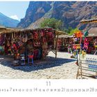11; Inkamarkt in Ollantaytambo. Marktstände mit bunten Textilien und Taschen vor einer Bergkulisse.