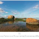 „Meeresstille“, Monatskalender für November. Große Felsen im klaren Wasser, umgeben von Schilf, unter blauem Himmel.