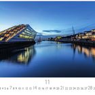 "Dockland", Novemberkalender. Modernes Gebäude mit stufenförmigem Design am Wasser in der Abenddämmerung.