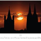 Text: "Sunset", "11". Silhouette einer Stadt mit Türmen vor einem orangefarbenen Sonnenuntergang mit Vogelschwarm.