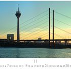 Text: "Düsseldorf, Rheinkniebrücke", Kalender mit Zahlen. 
Blick auf eine Brücke und Fernsehturm bei Sonnenuntergang.