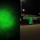 Links leuchtet ein grünes "U" auf Gras. Rechts steht "TROST" in grünen Lichtern auf Holzstapeln.