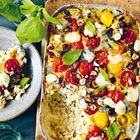 Bunter Auflauf mit Tomaten, geschmolzenem Käse und Nüssen, dekoriert mit Basilikumblättern auf Holzbrett.