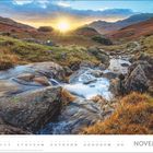 "NOVEMBER" und darunter ein Kalender. Im Vordergrund ein Bach, fließend über Felsen, umgeben von Gräsern. Sonnenuntergang im Hintergrund.