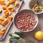 Gerösteter Kürbis, eingeweichte Bohnen, Salbeiblätter, Zitrone und Schale mit Mandeln und Kräutern auf einem Tisch.