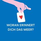 Der Text lautet: "WORAN ERINNERT DICH DAS MEER?" Eine Hand hält eine Karte mit einem roten Herz.