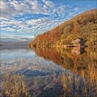Keine erkennbaren Texte. 

Eine Hütte am See mit herbstlichen Bäumen, ruhiges Wasser und Wolken am Himmel.