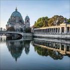Ein imposantes Gebäude mit einer grünen Kuppel spiegelt sich im ruhigen Wasser eines Flusses wider.