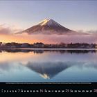 November 2023. Kalender mit Berg im Hintergrund, reflektiert in einem stillen See. Stimmungsvolle Farben, pastelliger Himmel.