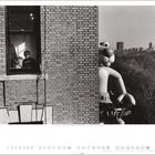 Zwei Personen am Fenster, Schriftzug „LIFEGUARD“ auf einem Ballon, Stadt im Hintergrund. Der Rand zeigt Kalenderzahlen.