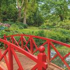 "Schutz durch Tallage" beschreibt einen Garten in Dorset. Eine rote Brücke überquert einen Teich im grünen, blühenden Garten.