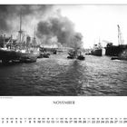 „Versmannkai des Baakenhafens“, „NOVEMBER“. Schiffe im Hafen, Rauch steigt auf, Kräne und Wasser umgeben sie.