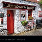 Ein irisches Pub mit der Aufschrift "An Teach Beag". Vor dem weißen Gebäude stehen alte Fahrräder und Fässer.