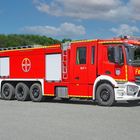 Feuerwehrfahrzeug, Seitenansicht, rot mit gelben Details. Aufschrift „BAYER“, „SLF-1“. Klarer Himmel, grüner Hintergrund.
