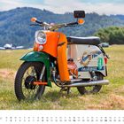 "Simson Freunde Falkensee" auf einem orange-grünen Moped in einer Wiese, mit Berglandschaft und Flugzeug im Hintergrund.