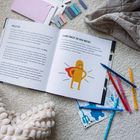 Links "HALLO DU!", rechts "WANN FÜHLST DU DICH MUTIG?". Gelbes Monster mit rotem Umhang, Buntstifte um Buch.