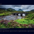 "07 Juli" und Monatskalender. Steinbrücke über Fluss in grüner Landschaft, Berge im Hintergrund, bewölkter Himmel.