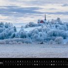 Norwegen 11. Winterlandschaft: Ein rotes Gebäude mit Turm auf einem Hügel, umgeben von verschneiten Bäumen und Feldern.
