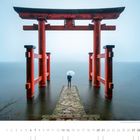 "Tori des Hakone Schreins am Ashi See, Hakone, Präfektur Kanagawa." Eine Person mit Regenschirm geht durch ein rotes Torii am Wasser.