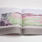 Ein aufgeschlagenes Buch zeigt eine Illustration mit schlafenden Menschen in grünen, roten und violetten Tönen.