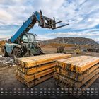 Kalender mit Daten, darunter ein blauer Kran, der gelbe Metallträger hebt, auf einer Baustelle mit Bergen im Hintergrund.