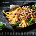 Kalendertage und Zahlen am unteren Rand. Pommes mit Käsesauce, Fleisch und grüner Paprika auf einem Blech.