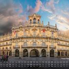 Text: "Plaza Mayor, Madrid 11" und ein Kalenderraster. Architektur: Elegantes Gebäude mit Bögen und Flaggen, abendlicher Himmel.
