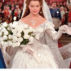 „DEZEMBER“ steht unten. Eine Frau im eleganten weißen Kleid mit Blumenstrauß; hinter ihr eine Menschenmenge.