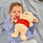 Ein Baby liegt auf einer grauen Decke, hält ein Kuscheltier und kaut auf einem roten Beißring.