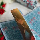 Ein Buch zeigt ein Bild einer nachdenklichen Frau. Der Hintergrund hat rote, herzförmige Blumenmuster und Blätter.