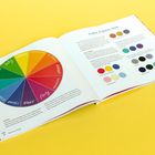 Eine aufgeschlagene Broschüre zeigt ein Farbkreis-Diagramm mit Emotionen wie "HAPPY" und "RELAXED" in verschiedenen Farben.