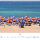 Text: "Caleta de Fuste", "12", "CASARES EDITION". Strand mit orange-blauen Sonnenschirmen und Liegestühlen, Meer im Hintergrund.