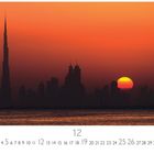 Dubai Skyline im Sonnenuntergang, Kalender für Dezember, orangener Himmel, Sonne hinter Wolkenkratzern, reflektierende Wasseroberfläche.