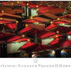 Weihnachtsmarkt. Zahl 12. Weihnachtsmarktstände mit roten Dächern, beleuchtet mit Lichterketten und Sternen.