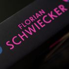 Der Text "FLORIAN SCHWIECKER" erscheint in leuchtendem Pink auf einem schwarzen Hintergrund.