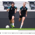 **DEZEMBER** unten. Zwei Fußballspielerinnen im schwarzen Trikot rennen. Rasen im Vordergrund, leere Tribünenplätze im Hintergrund.