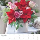 Kalender mit Monat Dezember, festlich geschmückt mit roten Blumen, Tannenzweigen und Tannenzapfen im Hintergrund.