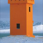 Dezember 12; ein oranger Leuchtturm auf schneebedecktem Gelände vor einem blauen Himmel.